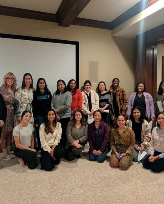WID event attendees pose in two rows in front of a projection screen after the presentation.