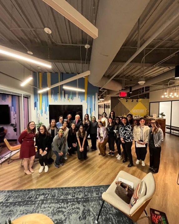 WID event attendees pose together in a modern meeting space, many wearing playful oversized glasses.